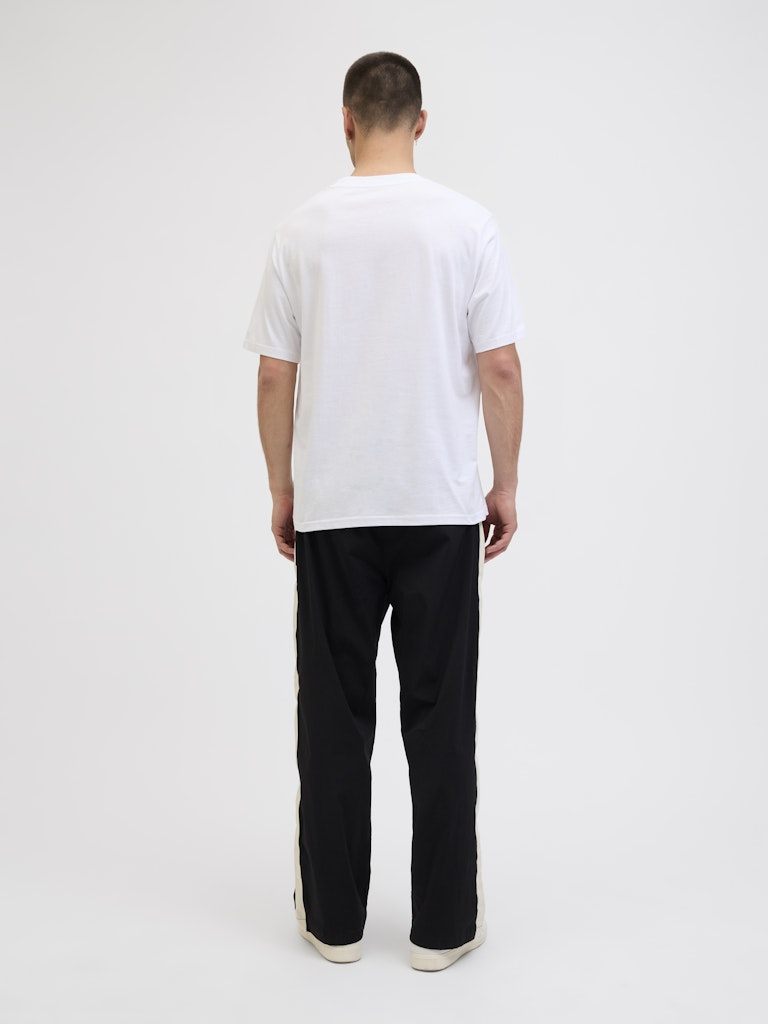 Person wearing a white t-shirt and black pants on a plain background