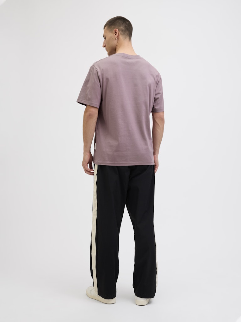 Man wearing a mauve t-shirt and black pants with a white stripe on a white background
