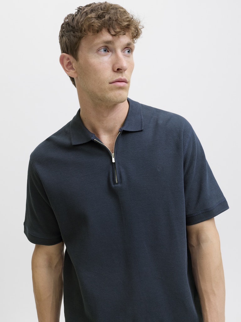 Man wearing a navy polo shirt against a plain background