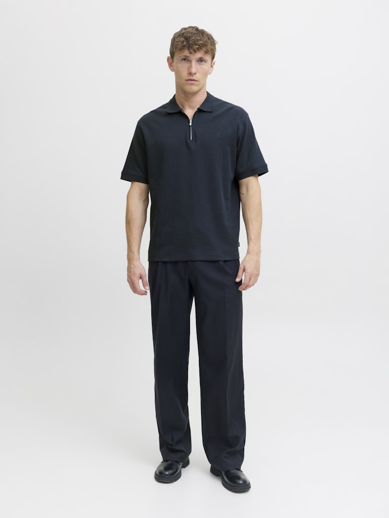 Man wearing a navy polo shirt and navy pants on a light gray background