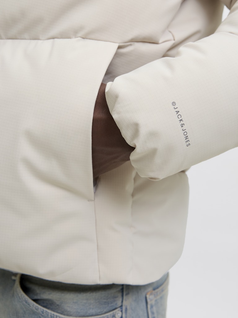 Close-up of a beige jacket with a brand logo on a light gray background