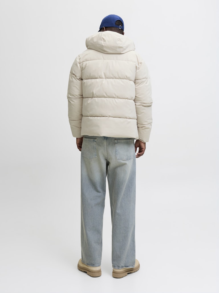 Person wearing a beige puffer jacket and light blue jeans on a white background