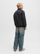 Side view of the junior boys black bomber jacket with blue jeans