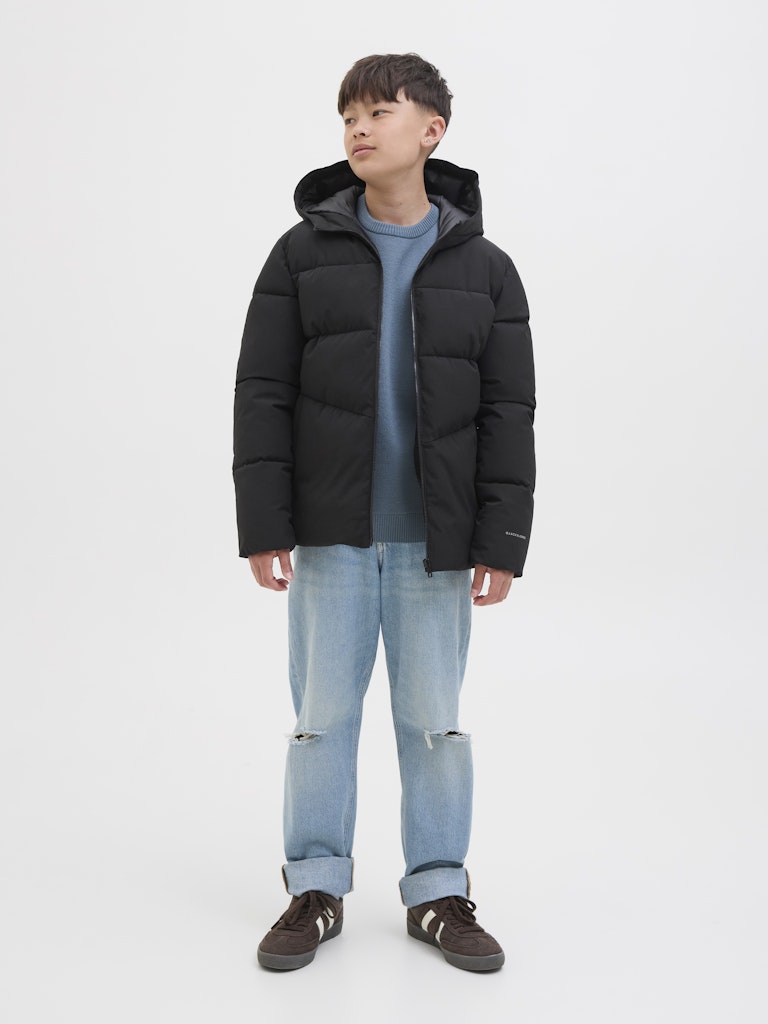Person wearing a black puffer jacket, light blue jeans, and dark shoes on a white background