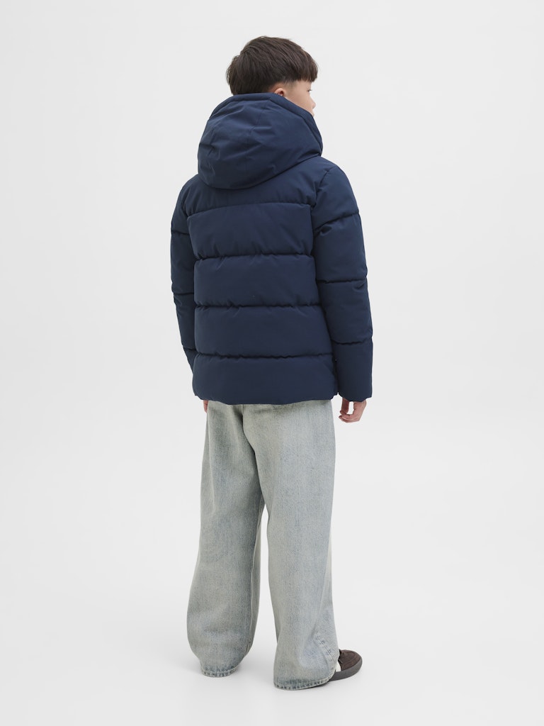 Person wearing a blue puffer jacket and gray pants on a white background