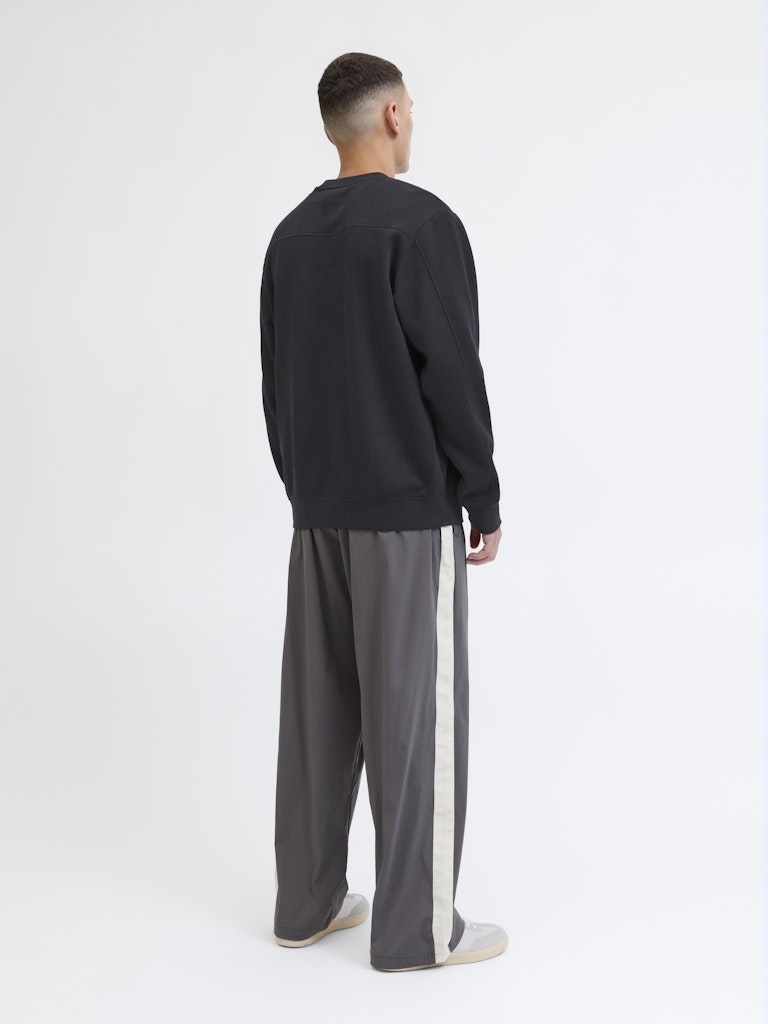 Person wearing a black sweater and gray pants with a white background