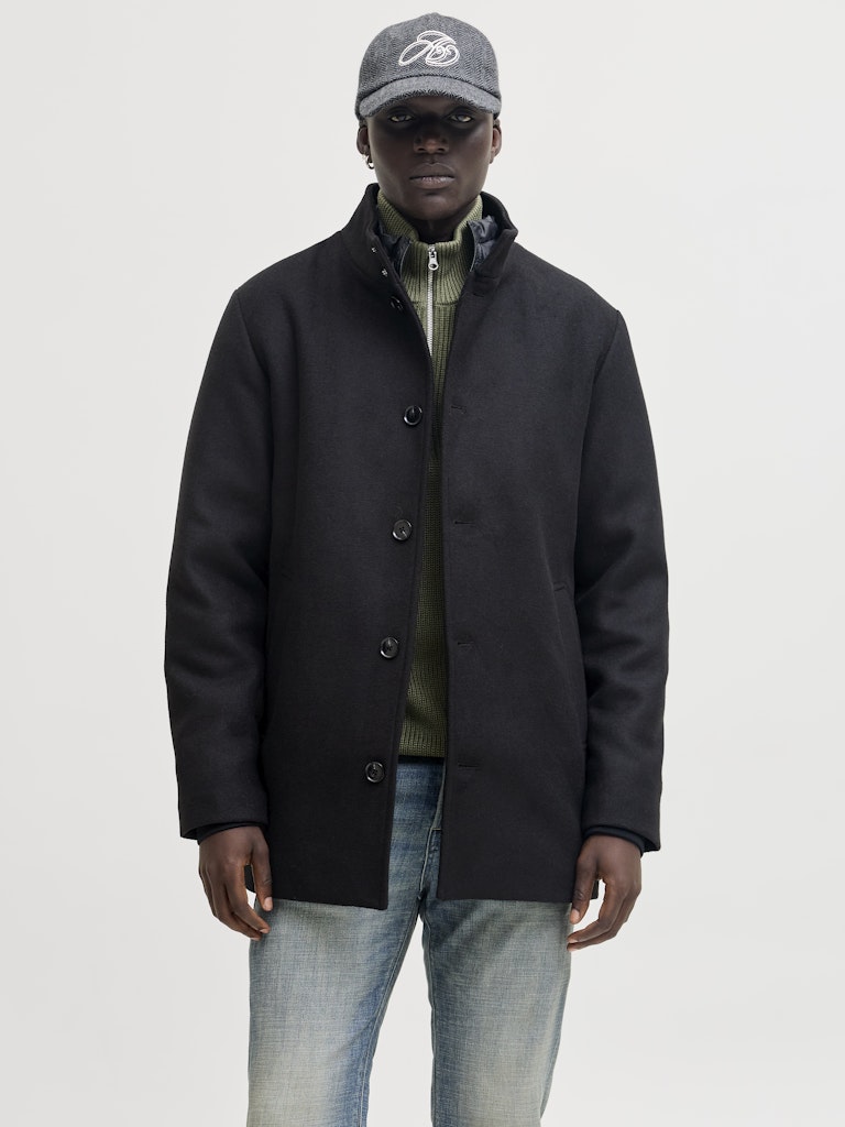 Man wearing a black coat, gray cap, and light blue jeans on a white background