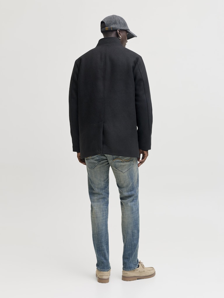 Person wearing a black coat and blue jeans on a white background