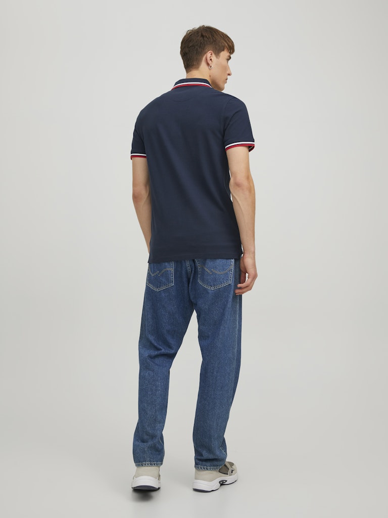 Person wearing a navy polo shirt and blue jeans on a white background