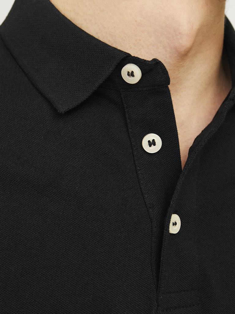 Close-up of a black polo shirt with white buttons on a plain background