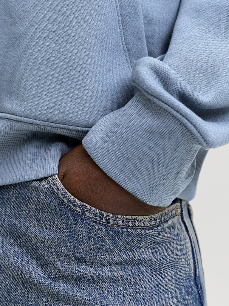 Light blue sweatshirt and jeans worn by a person, with a neutral background