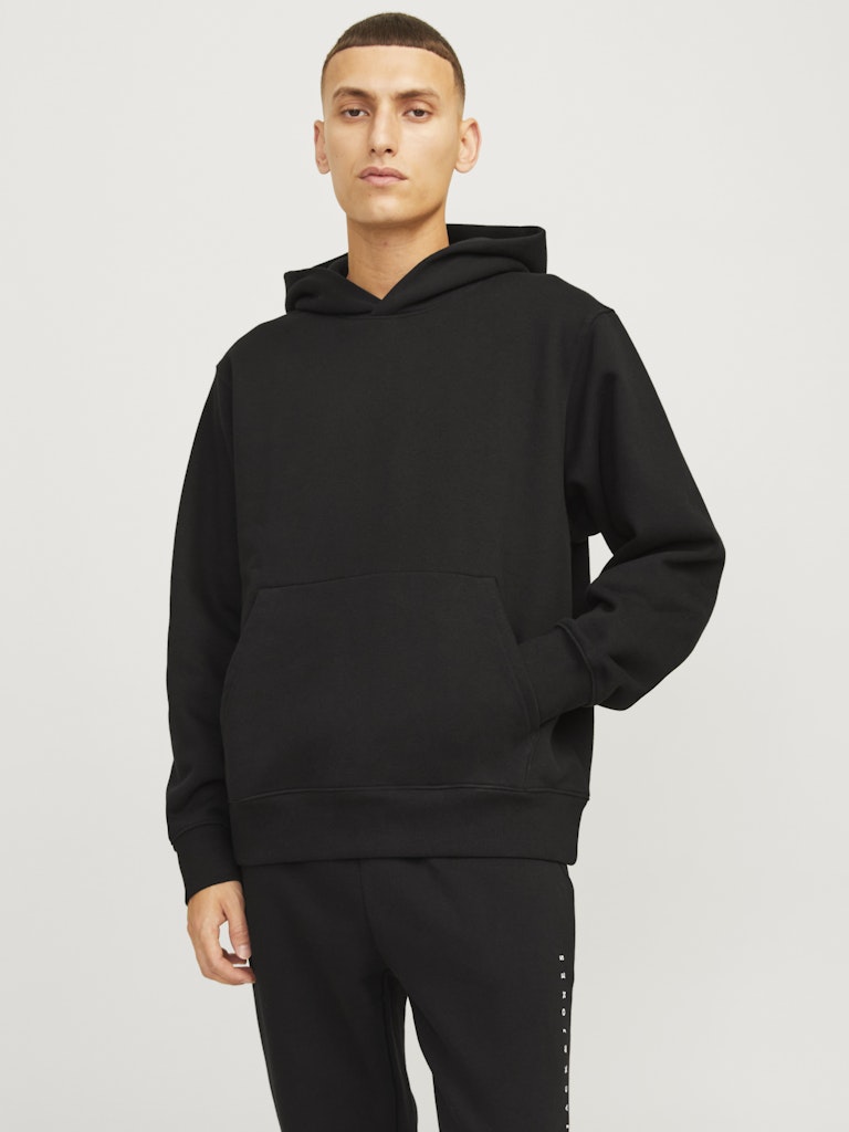Person wearing a black hoodie and pants on a light gray background