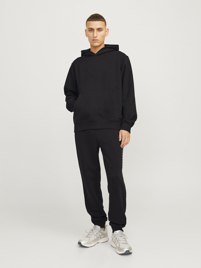 Person wearing a black hoodie and black pants on a white background