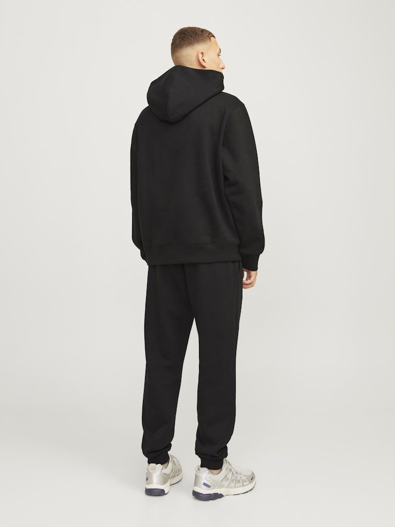 Person wearing a black hoodie and pants on a white background