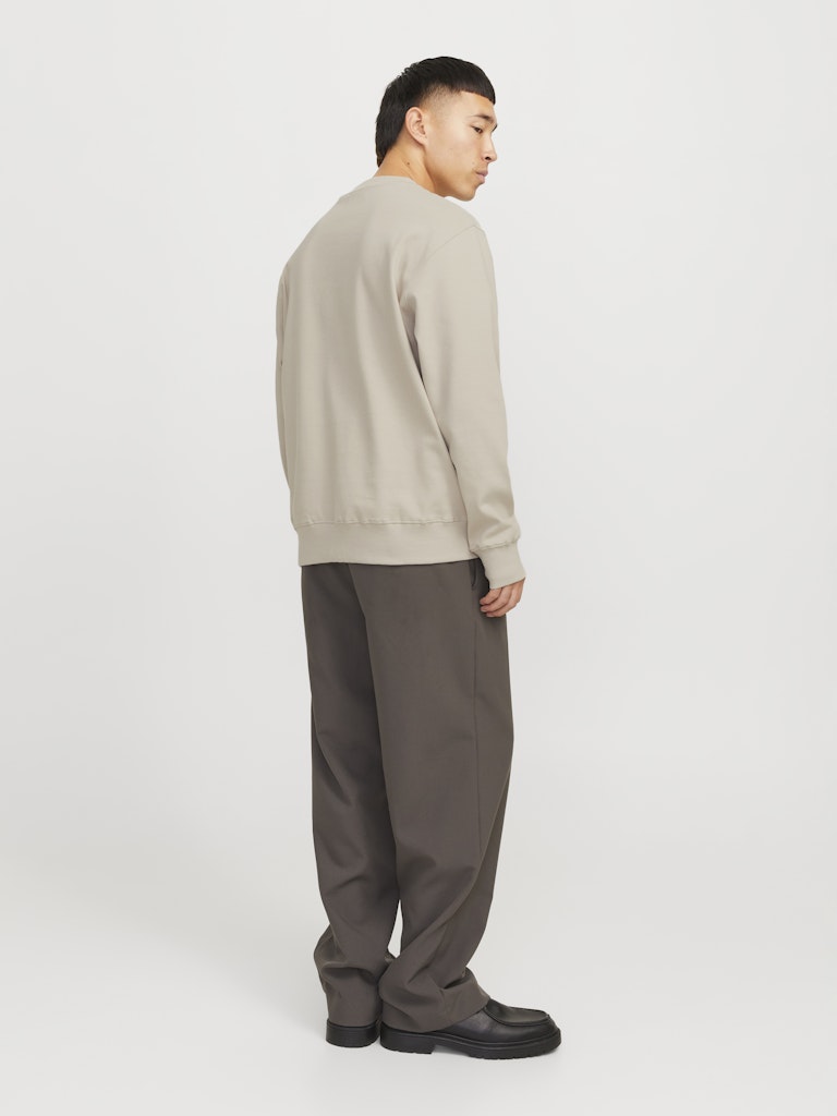 Person wearing a beige sweater and gray pants on a white background