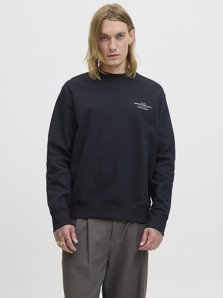 Person wearing a black sweatshirt with a small logo on a light gray background