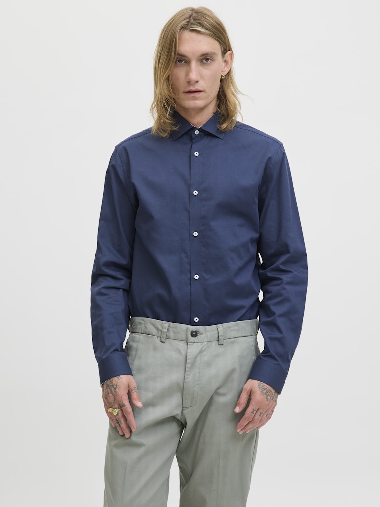 Man wearing a blue shirt and light gray pants on a white background