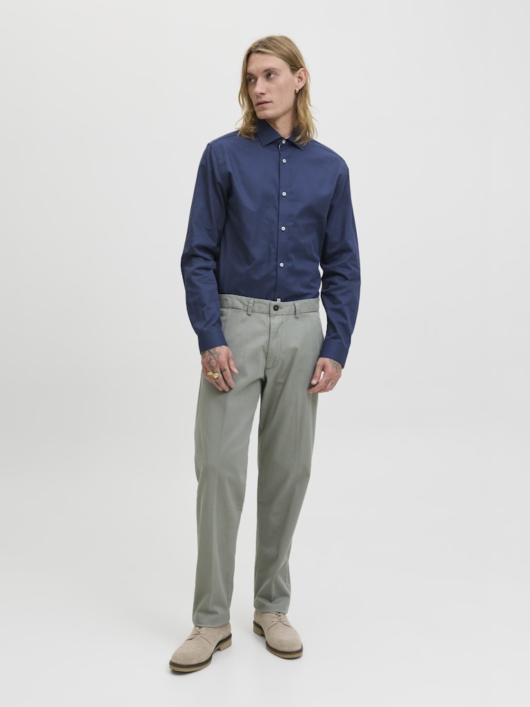 Man wearing a navy blue shirt and gray pants on a white background