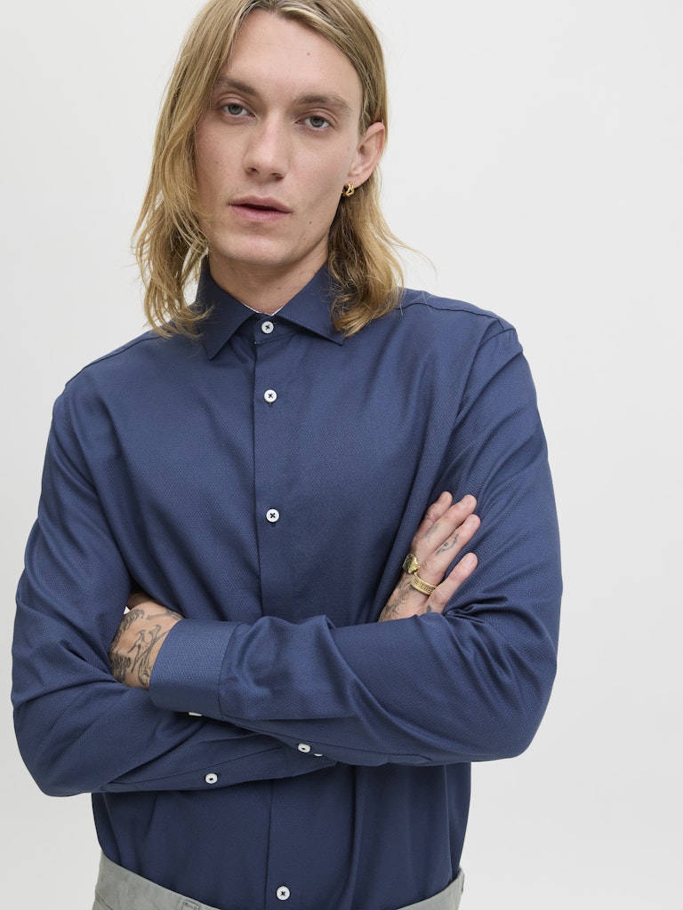 Man wearing a blue shirt with arms crossed against a plain background