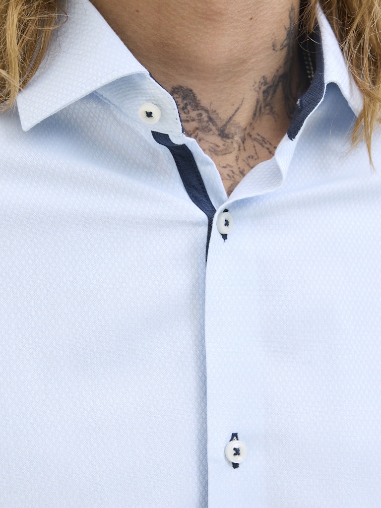 Close-up of a light blue shirt with white buttons and collar, featuring a tattoo on the neck.