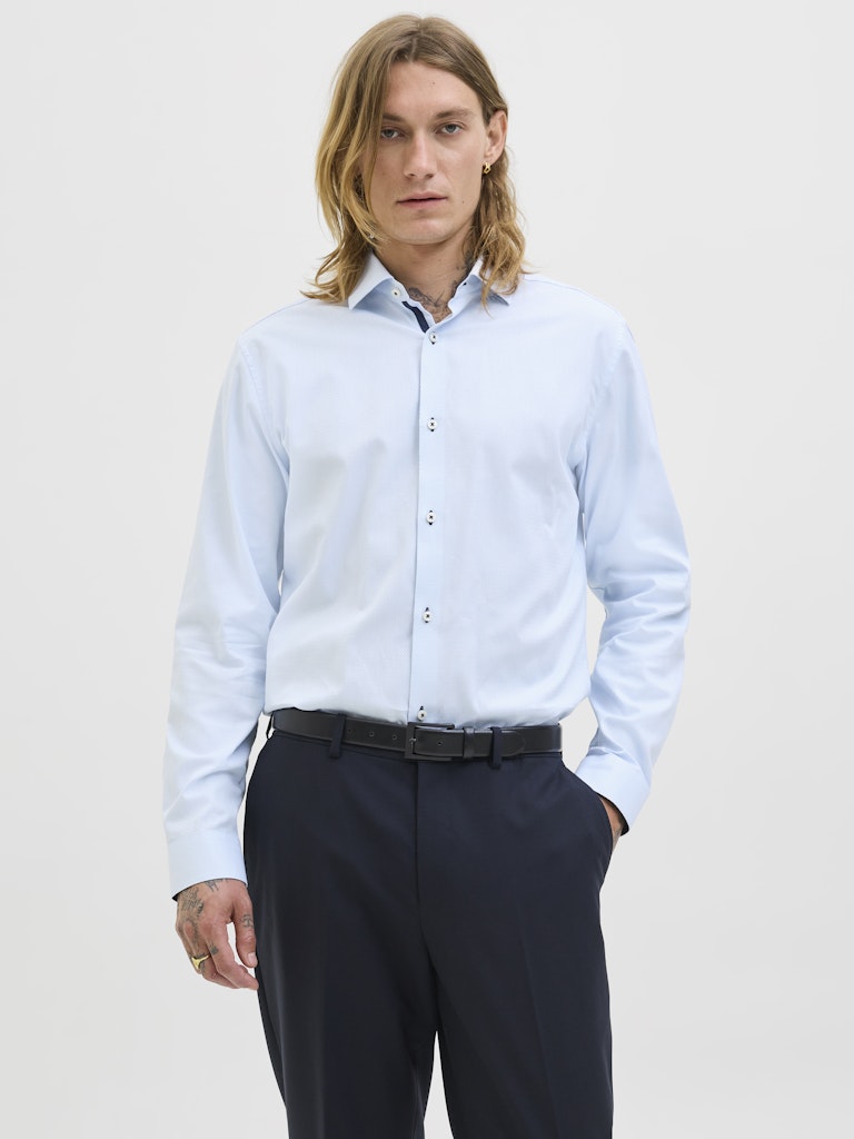 Person wearing a light blue dress shirt and dark pants on a plain background