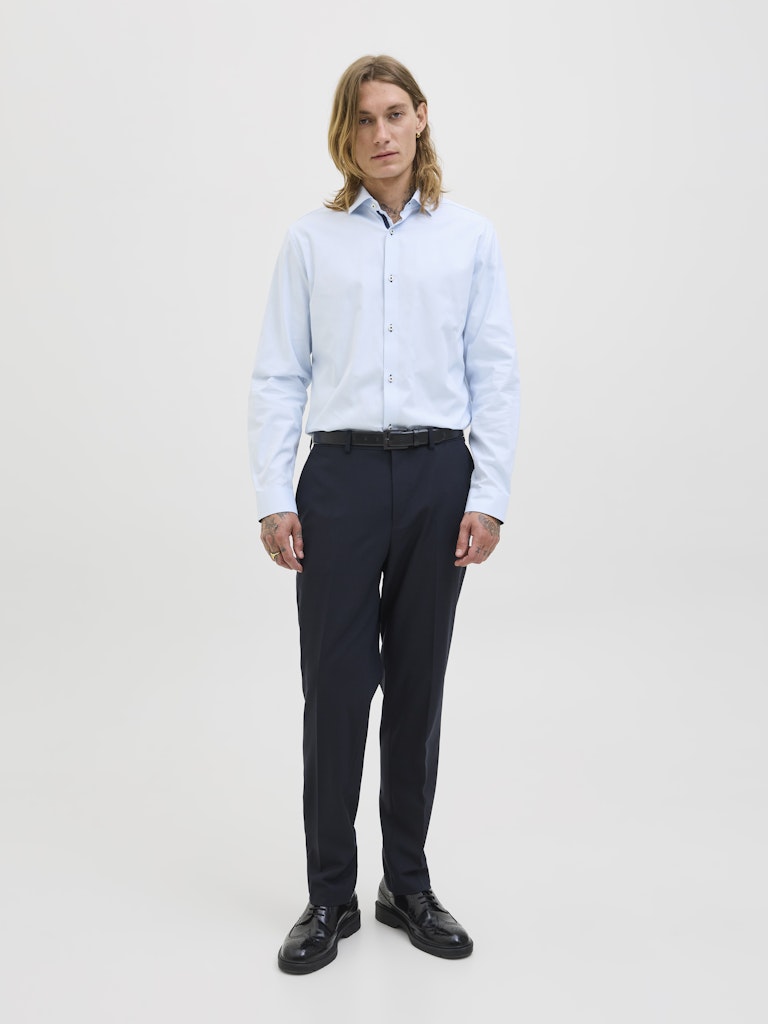 Man wearing a light blue shirt and dark pants on a white background