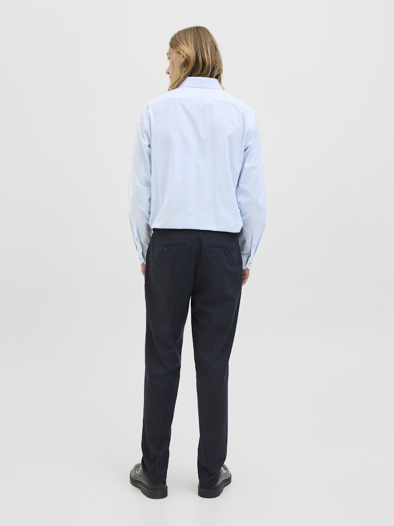 Person wearing a light blue shirt and dark pants on a plain background