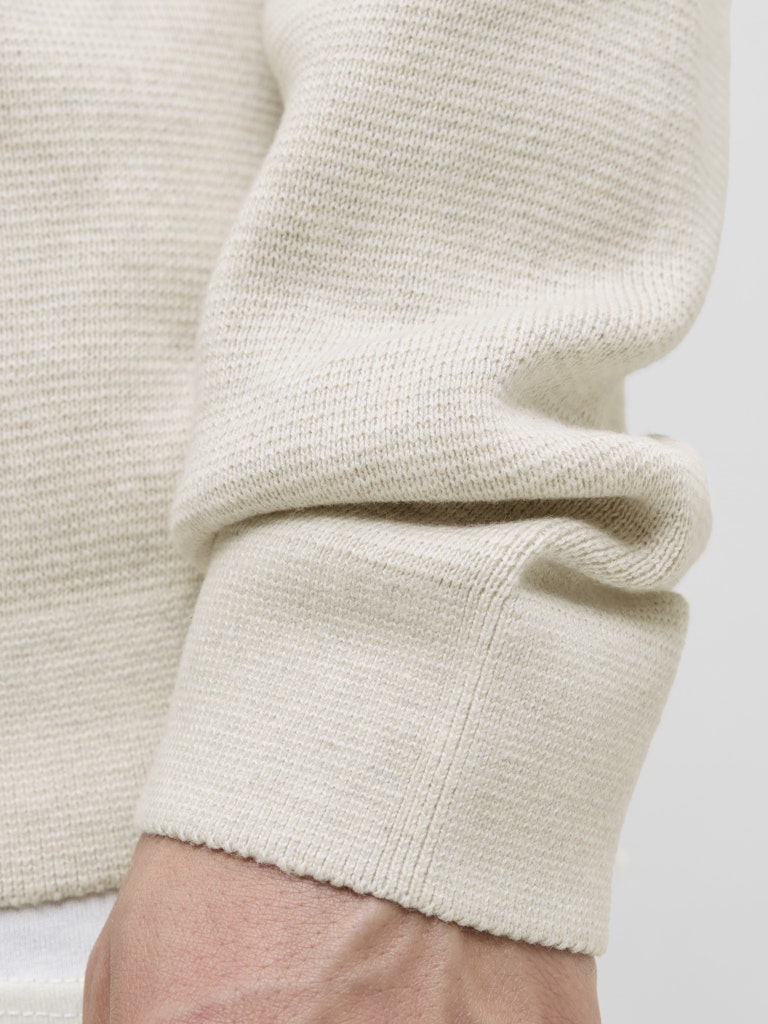 Close-up of a beige sweater sleeve on a plain background