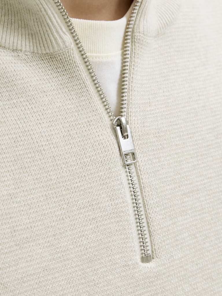 Person wearing a beige half-zip sweater against a plain background-Zip close up