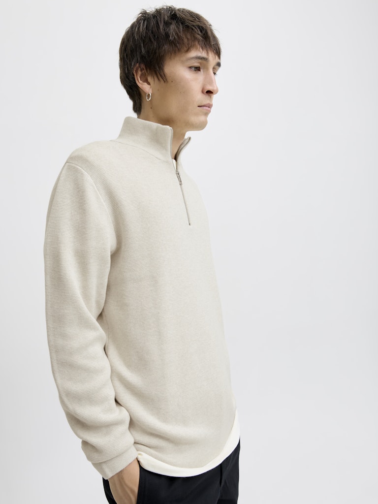 Person wearing a beige half-zip sweater against a plain background