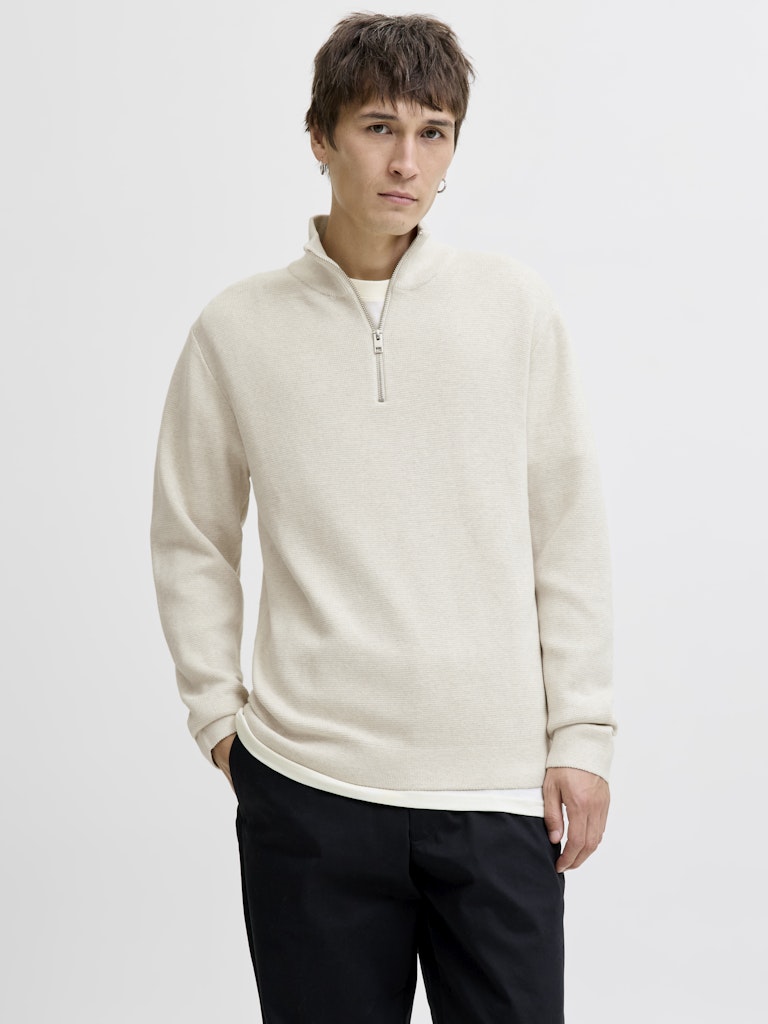 Person wearing a beige half-zip sweater against a plain background