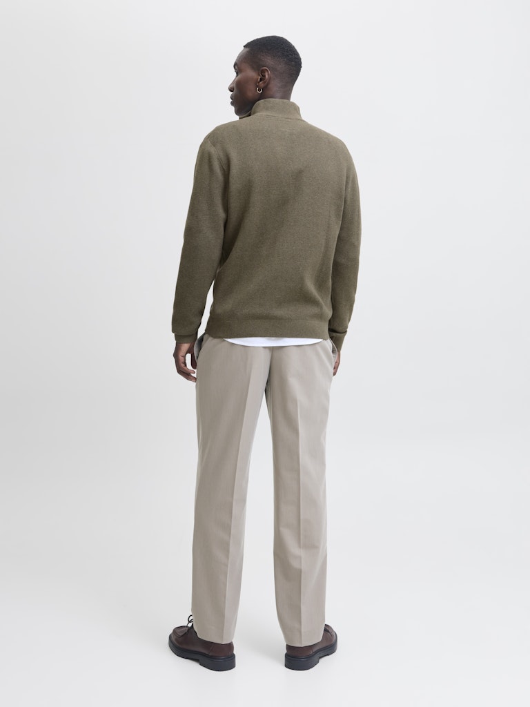 Man wearing a green sweater and beige pants on a white background