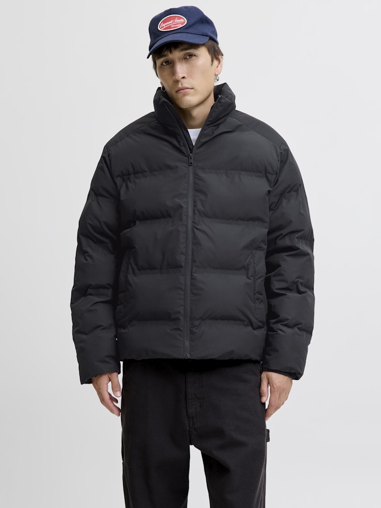 Person wearing a black puffer jacket and navy cap on a light gray background