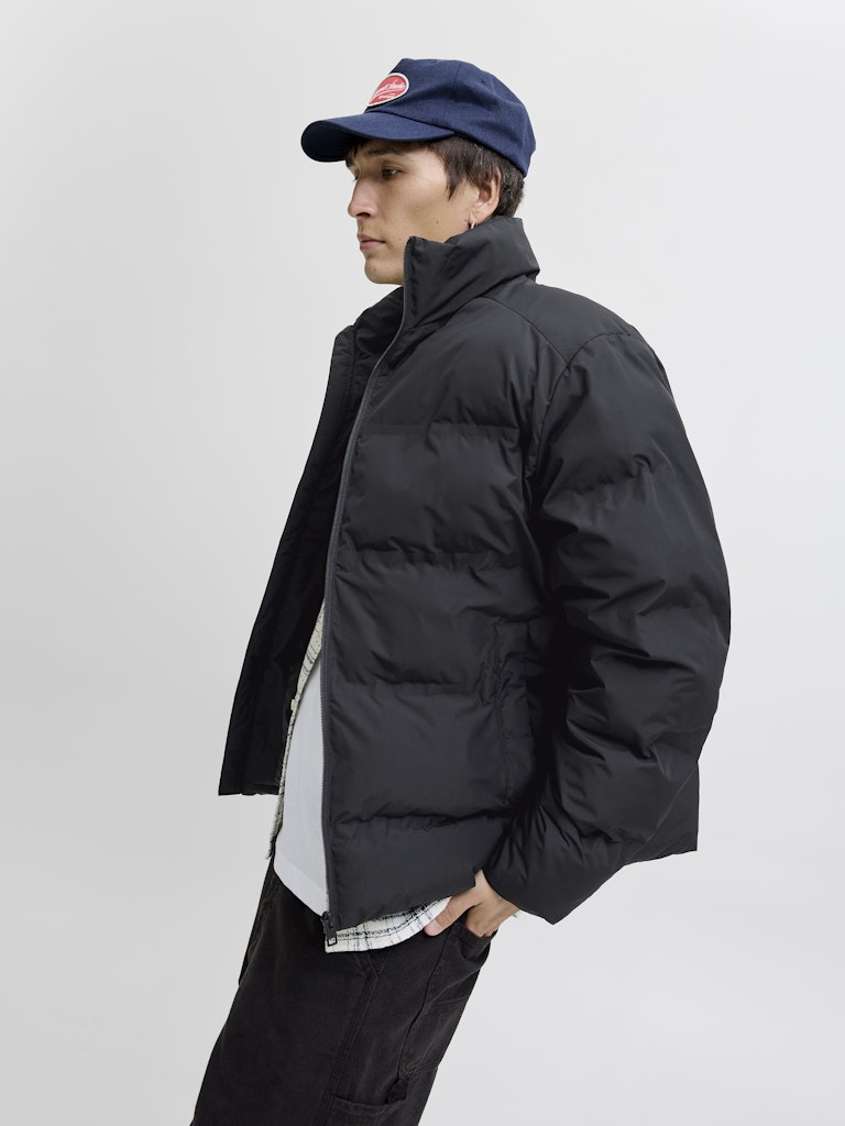 Person wearing a black puffer jacket and navy cap on a light gray background