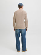 Person wearing a beige ribbed sweater and blue jeans standing against a white background