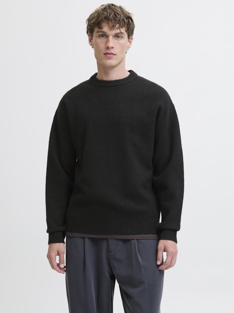 Man wearing a black sweater and gray pants on a light gray background