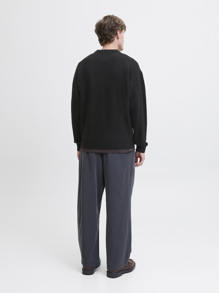 Person wearing a black sweater and gray pants on a white background