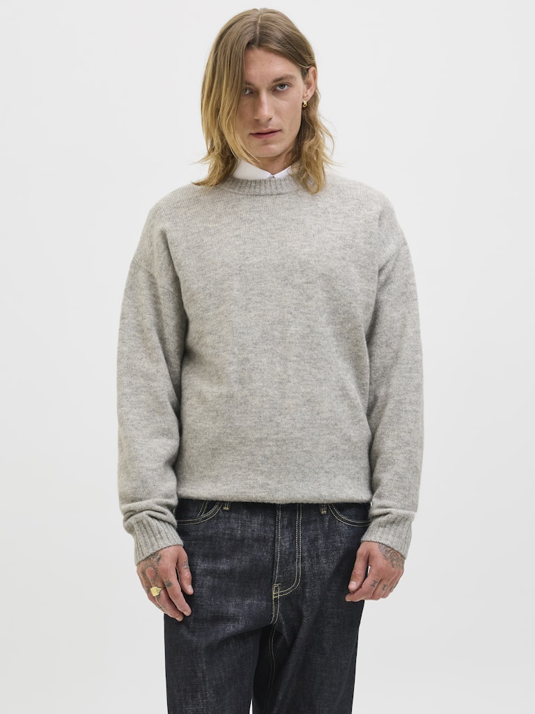 Person wearing a gray sweater and dark jeans on a white background