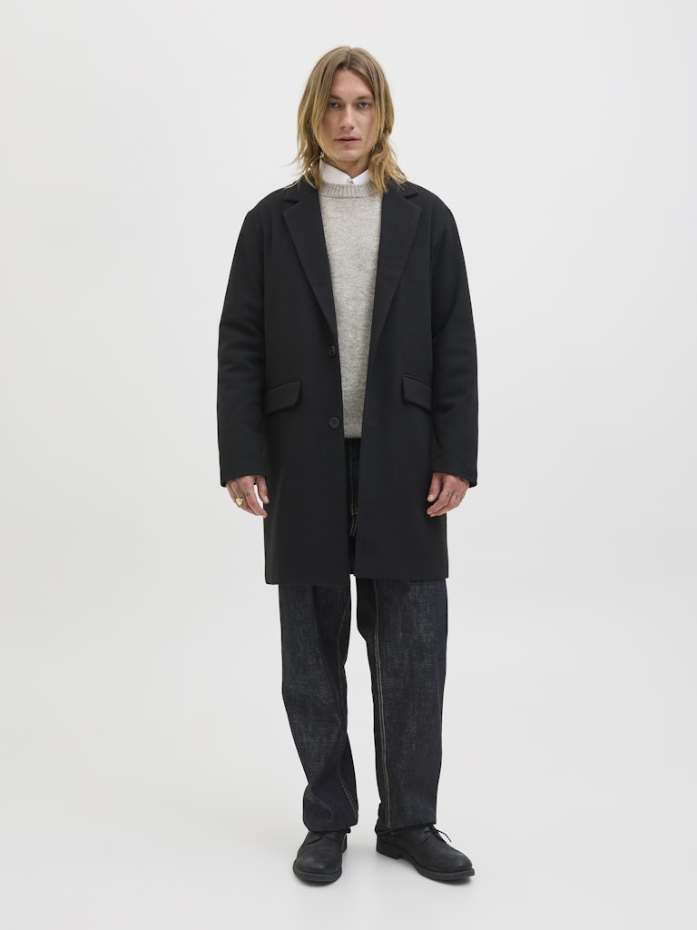 Person wearing a gray sweater under a black coat on a white background 