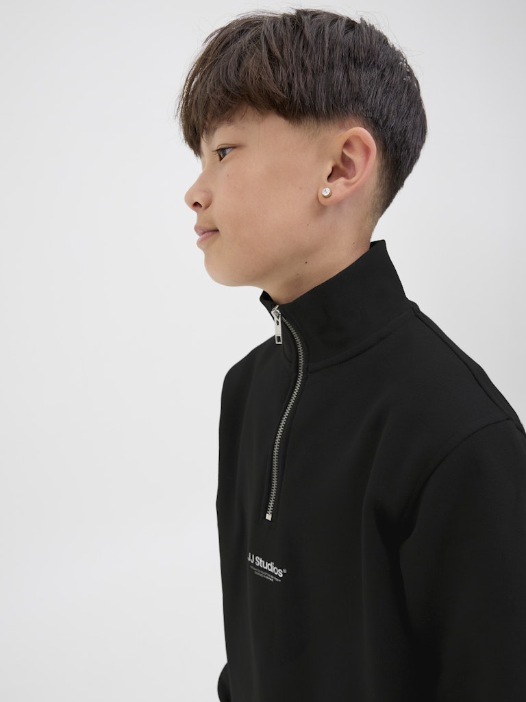 Person wearing a black high-neck sweater with a brand logo on a white background