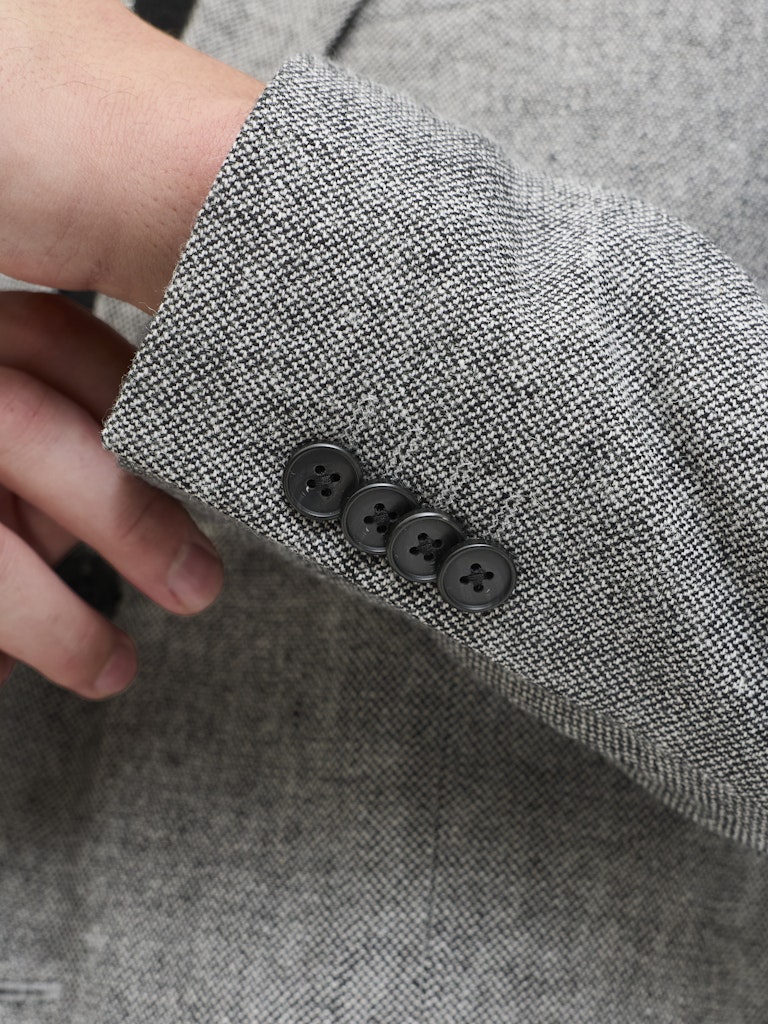 Close-up of a gray textured fabric with three black buttons, held by a hand.