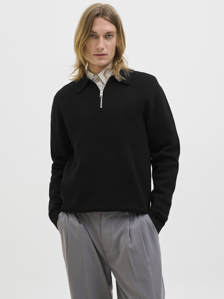 Person wearing a black polo sweater and light gray pants on a white background