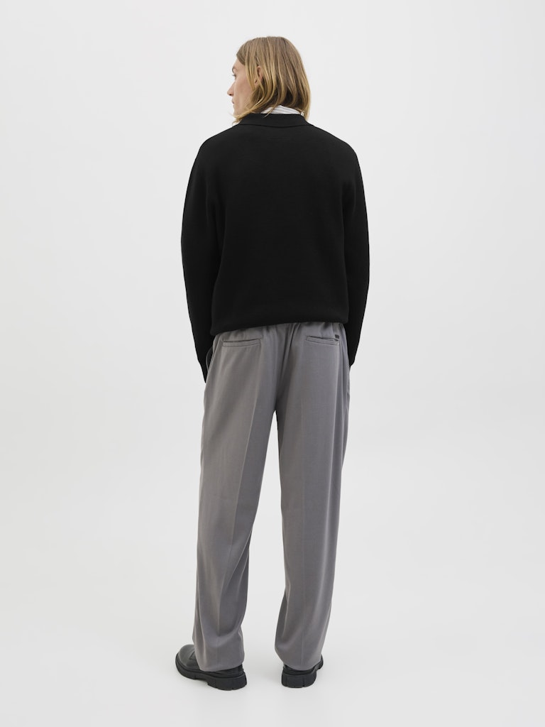 Person wearing a black sweater and gray pants on a white background