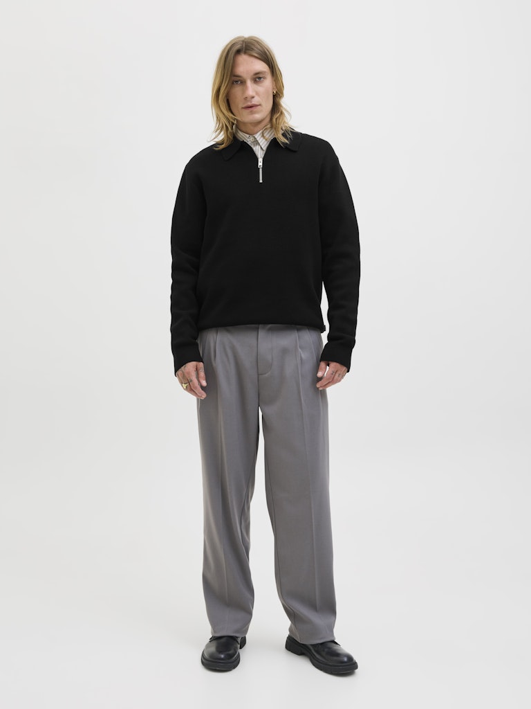 Man wearing a black  polo sweater and gray pants on a white background