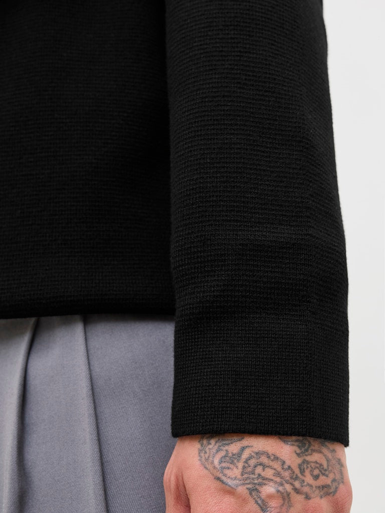 Close-up of a person wearing a black long-sleeve polo shirt with a tattoo on their arm.
