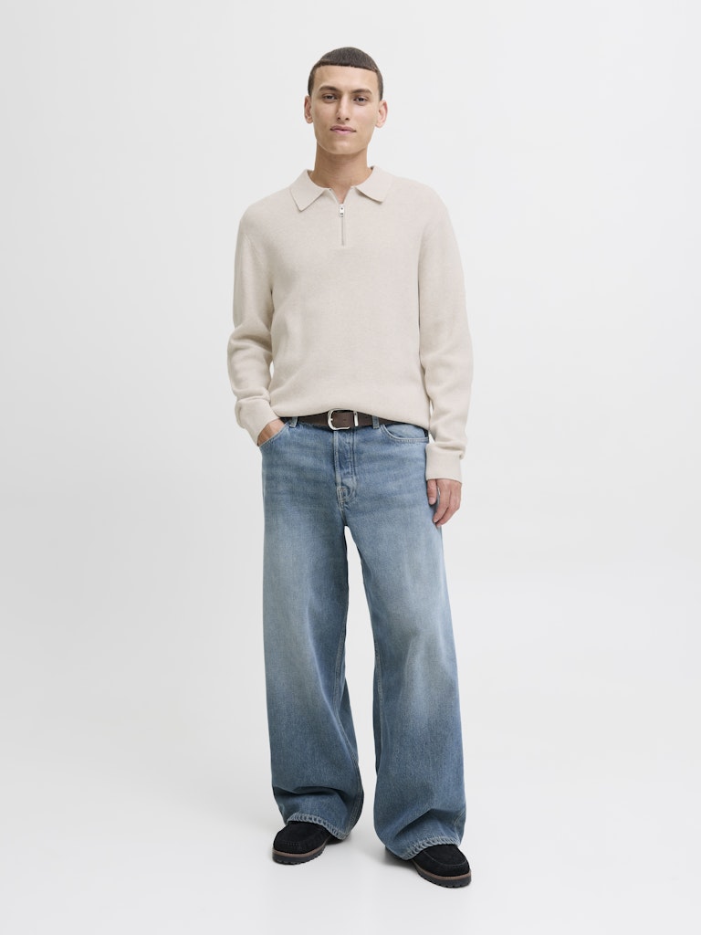 Man wearing a beige sweater and blue jeans on a white background