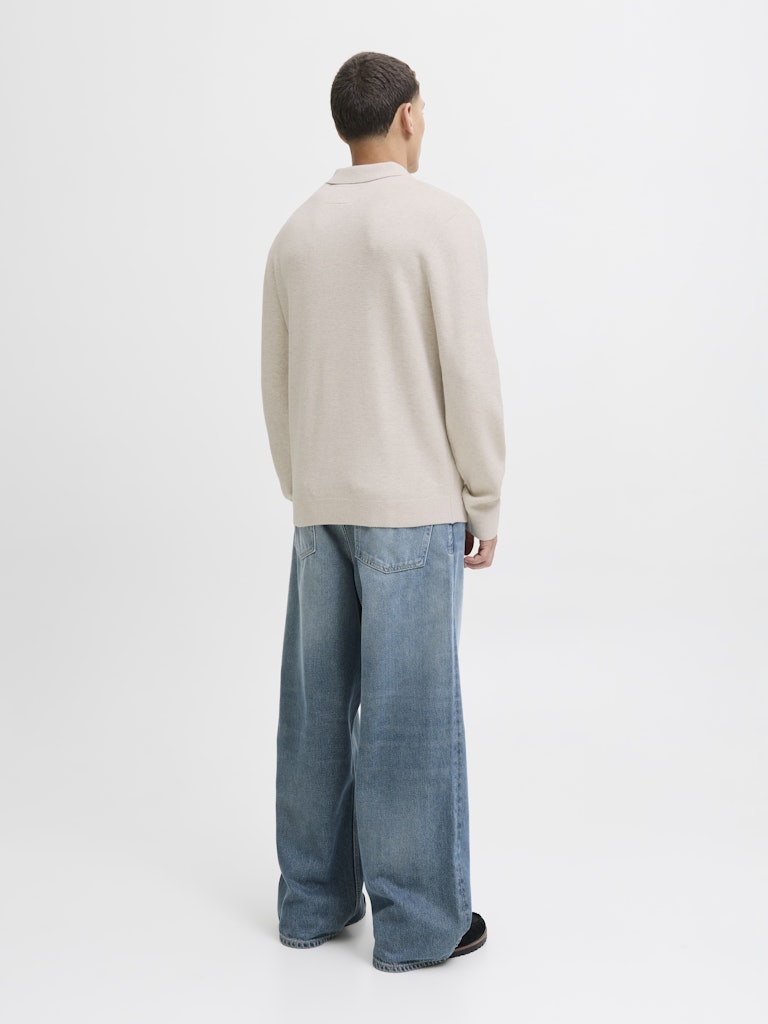 Person wearing a beige sweater and blue jeans on a white background