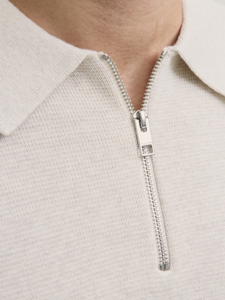Close-up of a light gray sweater with a silver zipper.