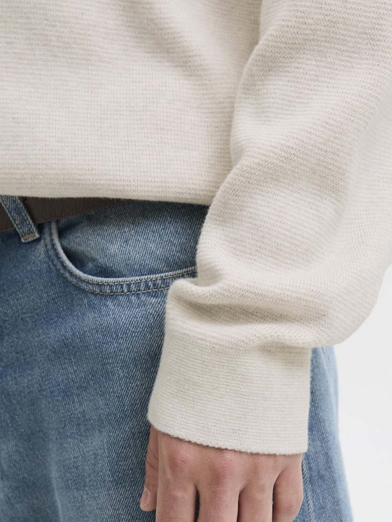 Close-up of a person wearing a beige sweater and blue jeans.