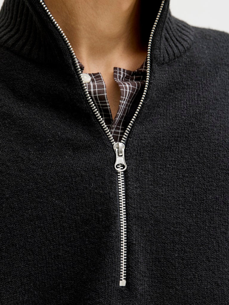 Close-up of a black sweater with a zipper, showing plaid shirt underneath. 